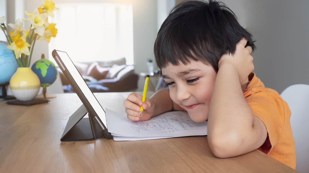 Image of a young smiling student doing online work on his tablet during COVID-19 lockdown